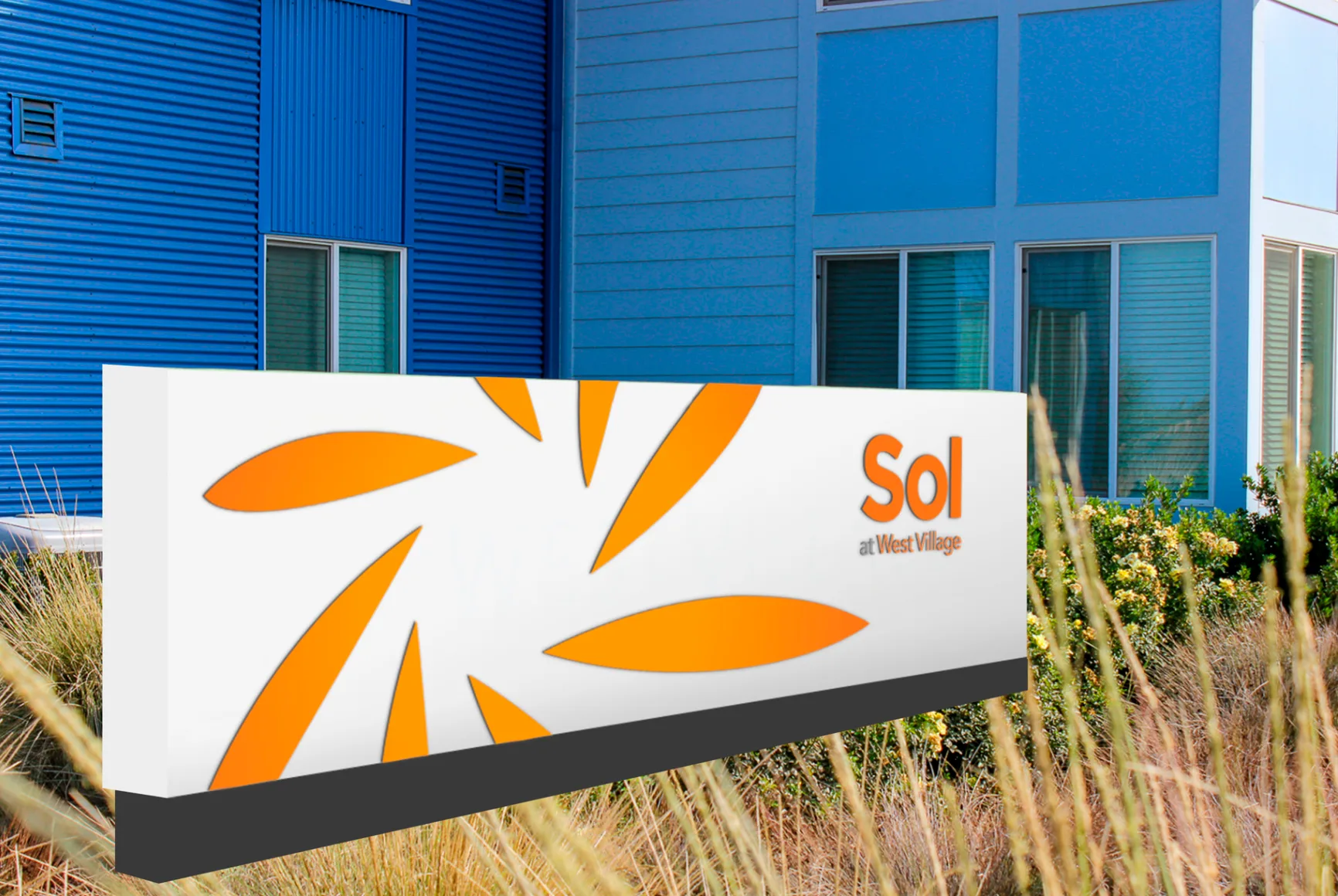 White exterior monument sign with an orange sunburst design and the Sol at West Village name outside a blue building