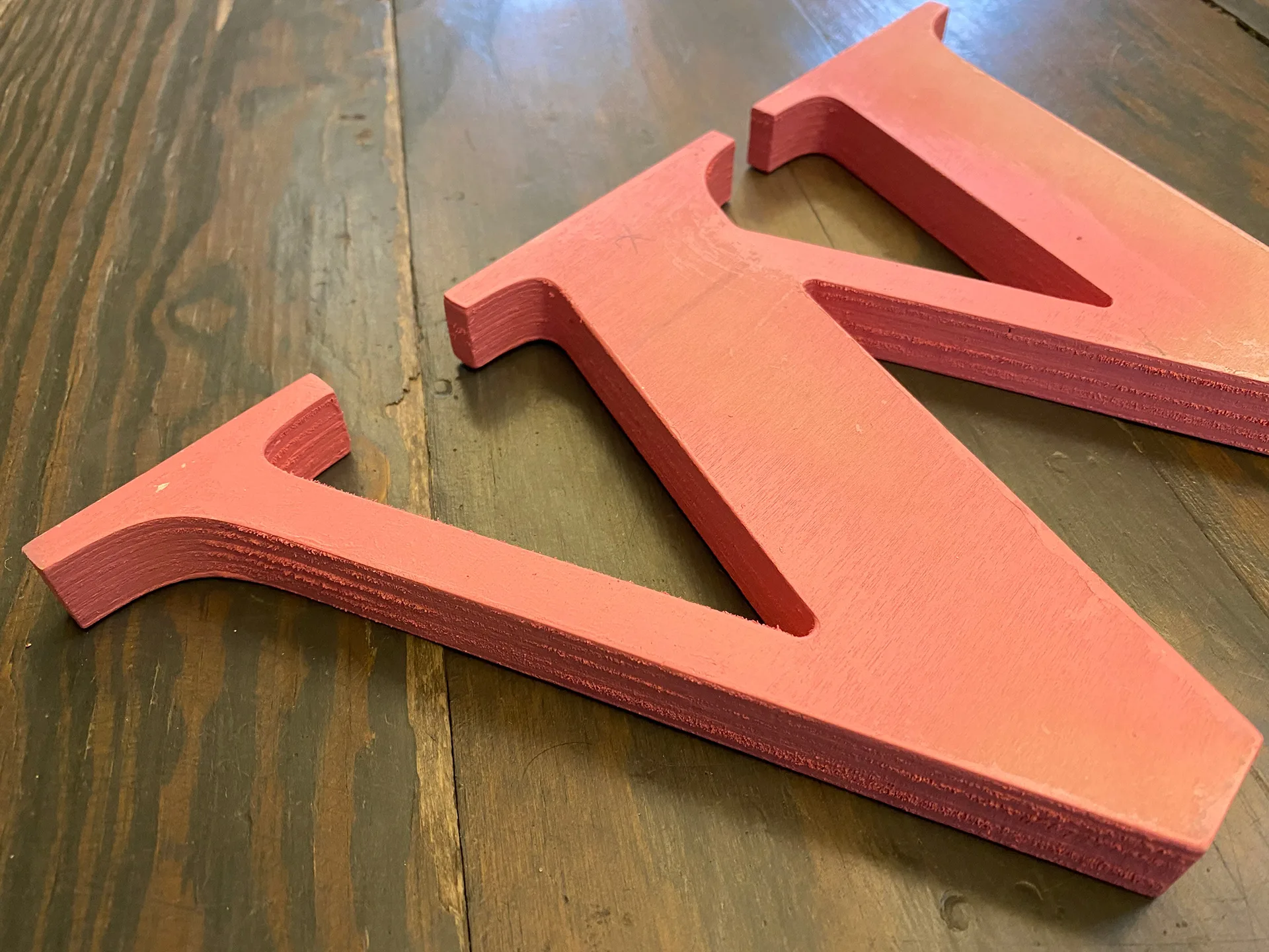 Fabricated dimensional letter W in coral paint resting on a wood workbench during signage production