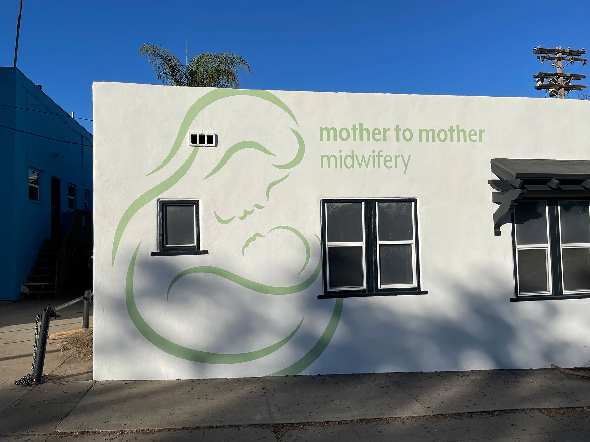 Mother to Mother Midwifery building facade with its green line-art logo of a mother cradling a child
