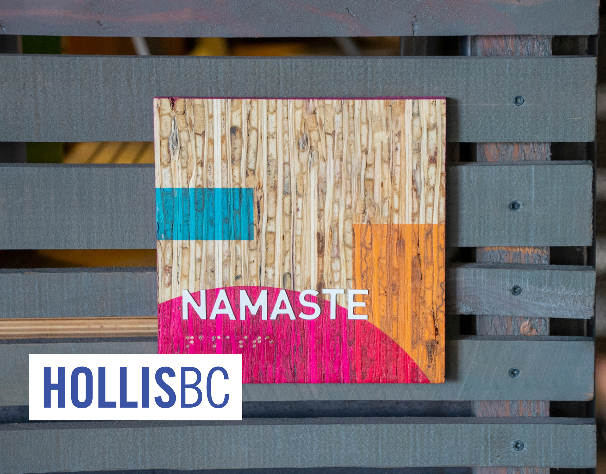 Colab Signage cover: wood sign reading Namaste with teal, orange, and pink color blocks against a slatted gray bench