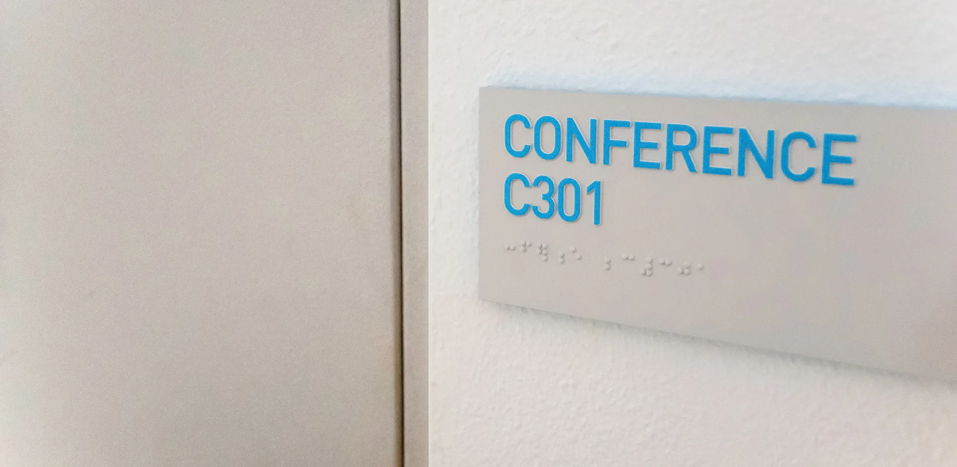 Conference room C301 wall sign in blue lettering on gray with braille dots below, mounted beside a doorway
