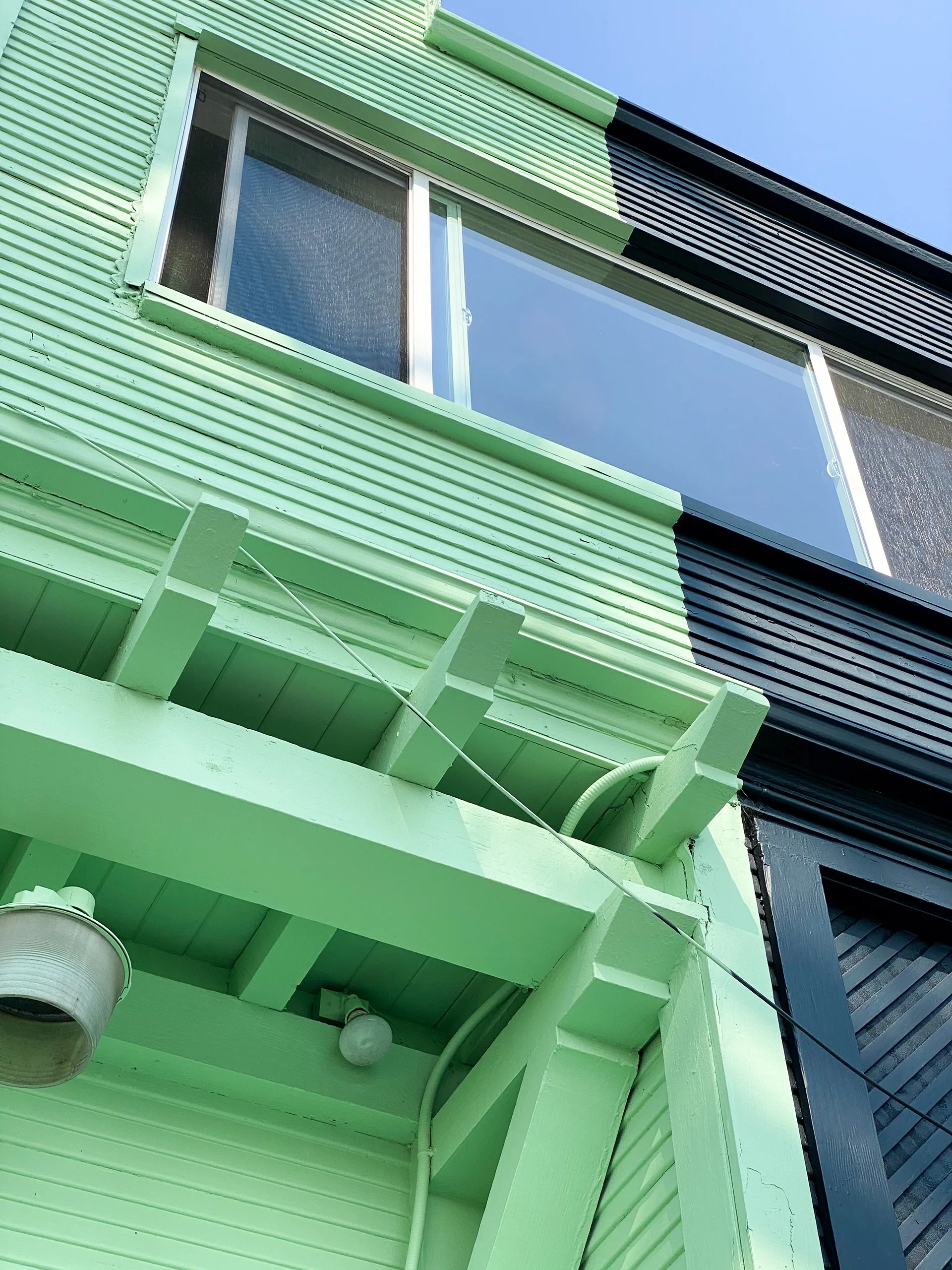 Close-up of the mint green building's cornice and window trim meeting the adjacent navy blue wall