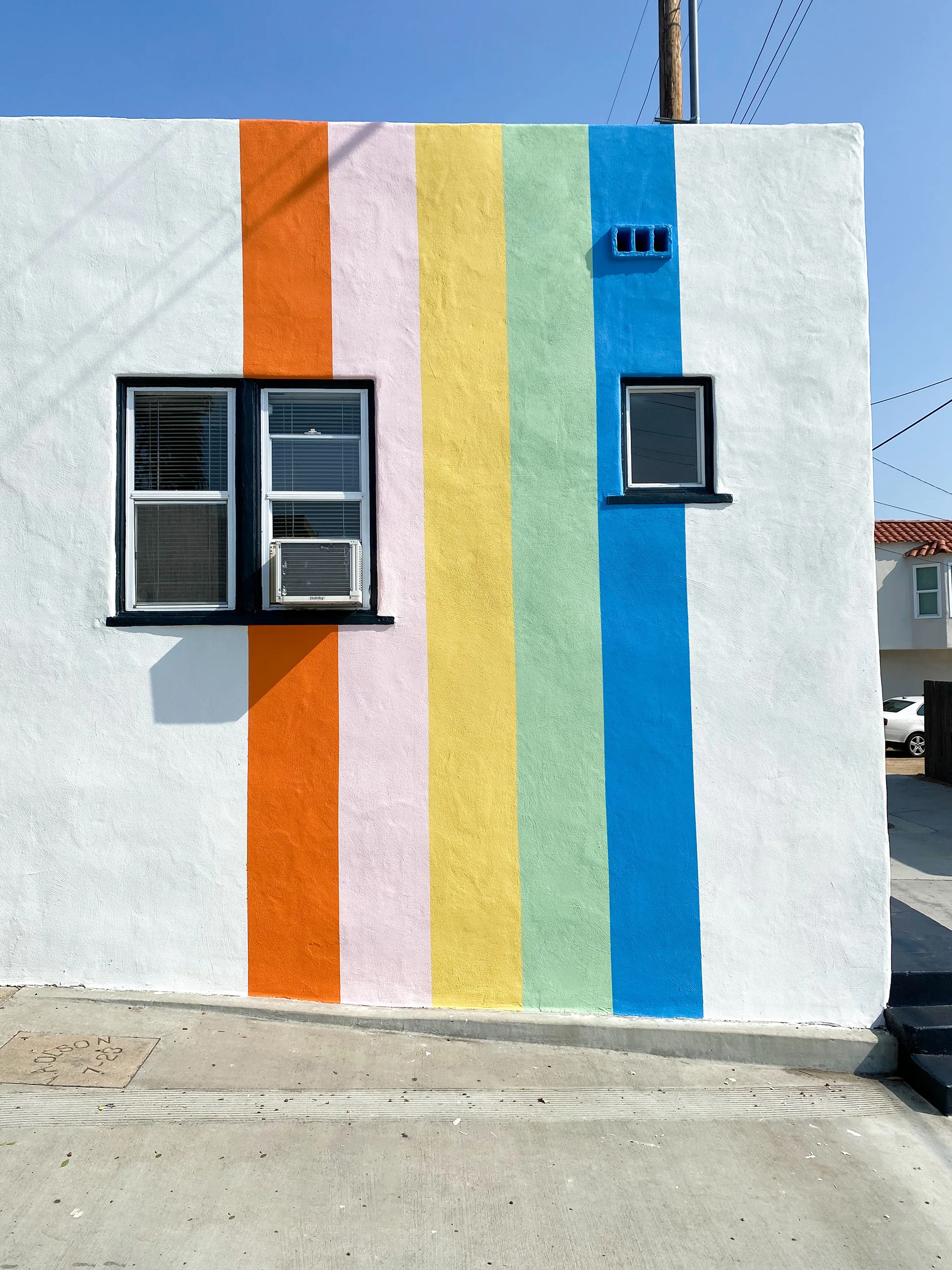 White building corner painted with orange, lavender, yellow, green, and blue vertical rainbow stripes flanking two windows