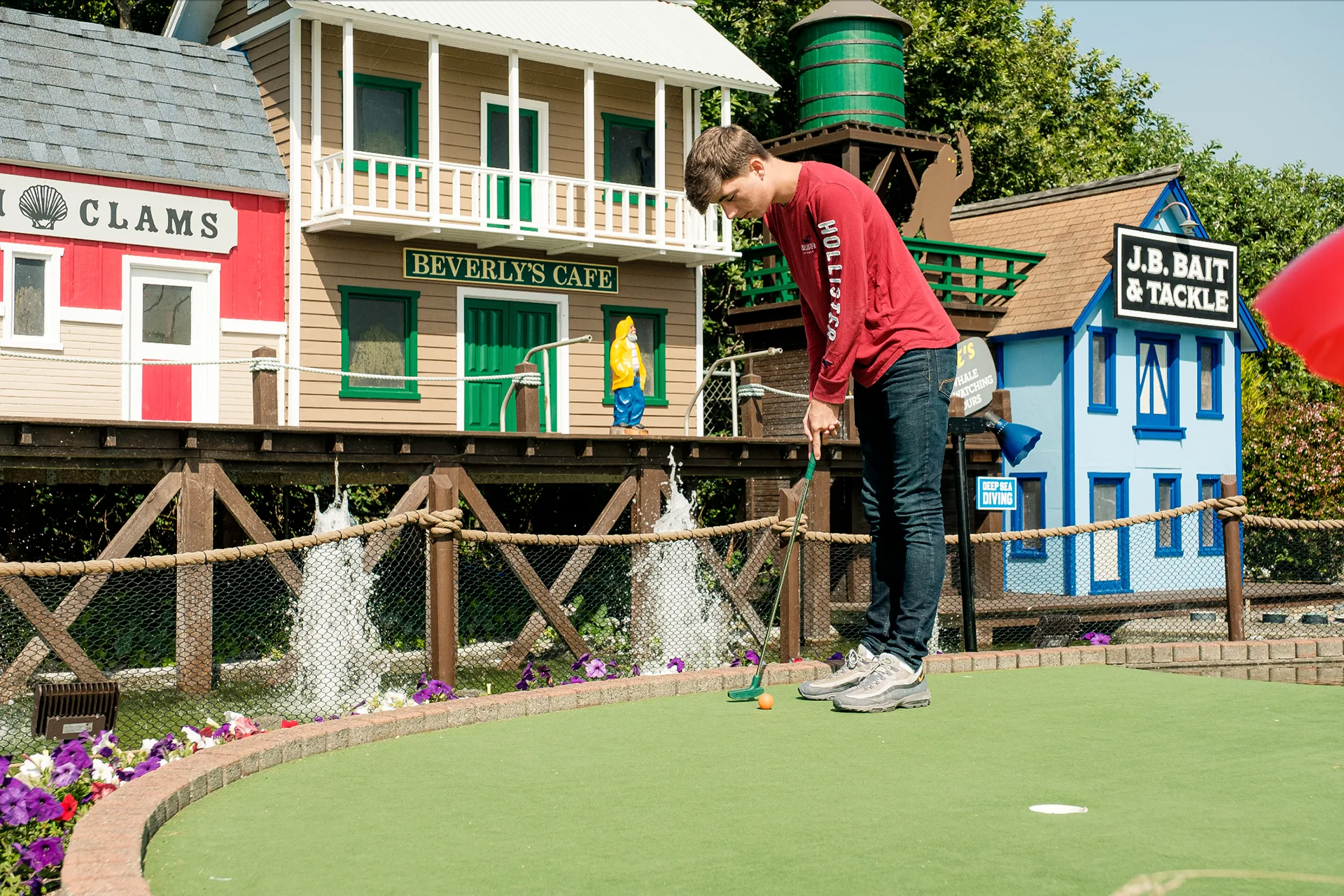 Golfer putting on the mini golf course in front of the Beverly's Cafe and J.B. Bait & Tackle village facades
