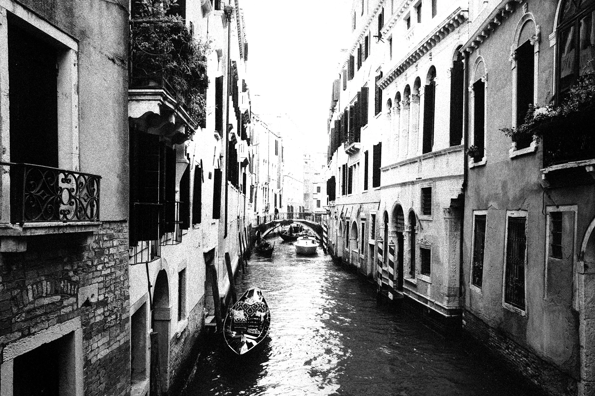 Black-and-white photo of a narrow Venice canal lined with historic buildings and a passing gondola