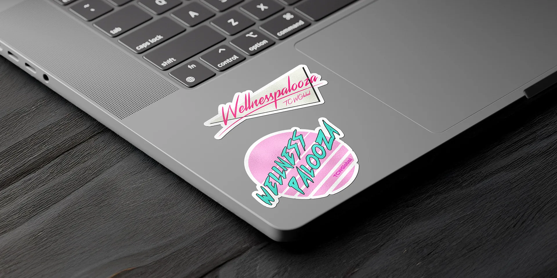 Wellnesspalooza pennant and circular badge stickers applied to the corner of a laptop's trackpad area
