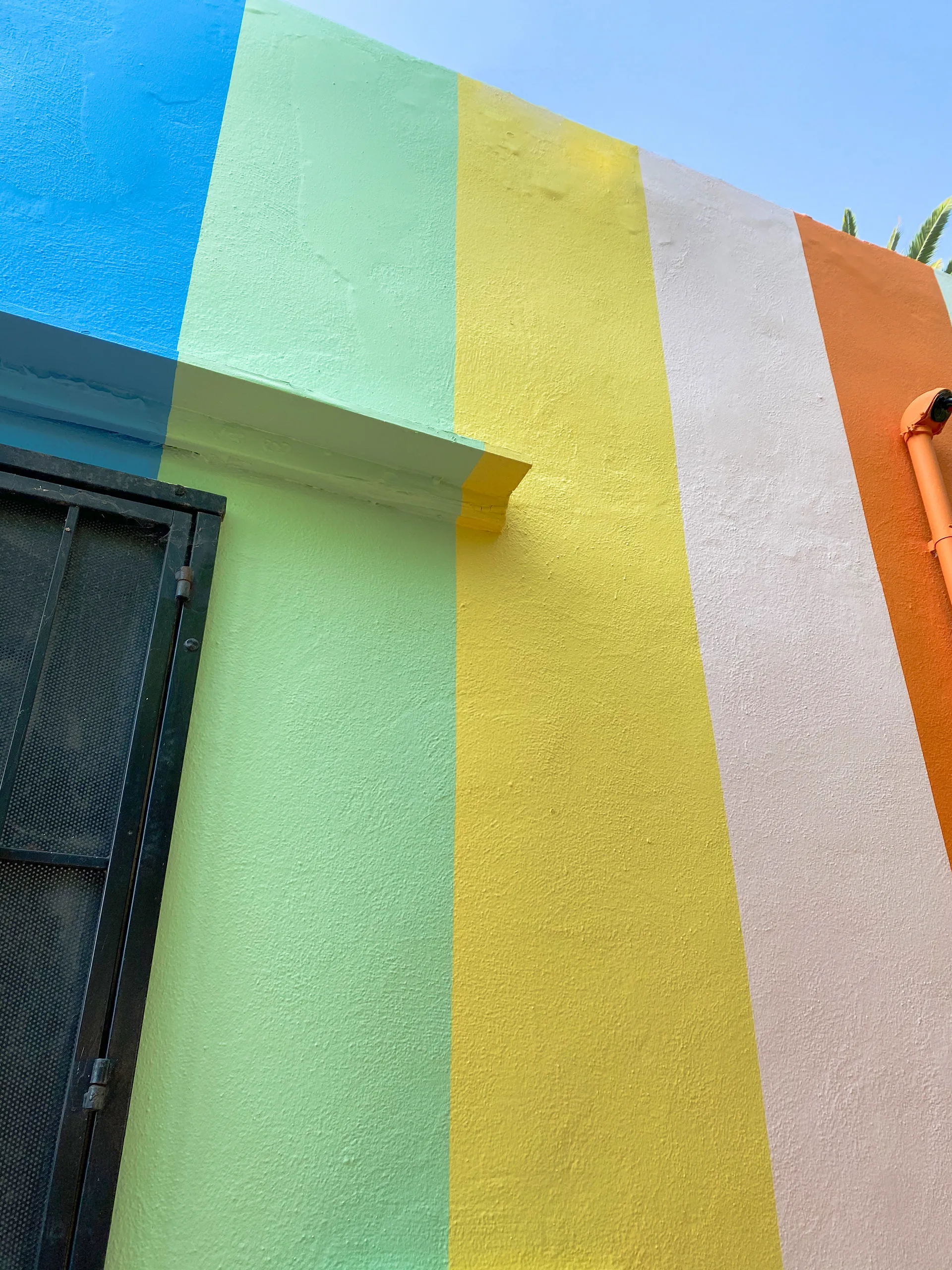 Close-up of the rainbow-striped wall corner meeting the roofline above a black security gate