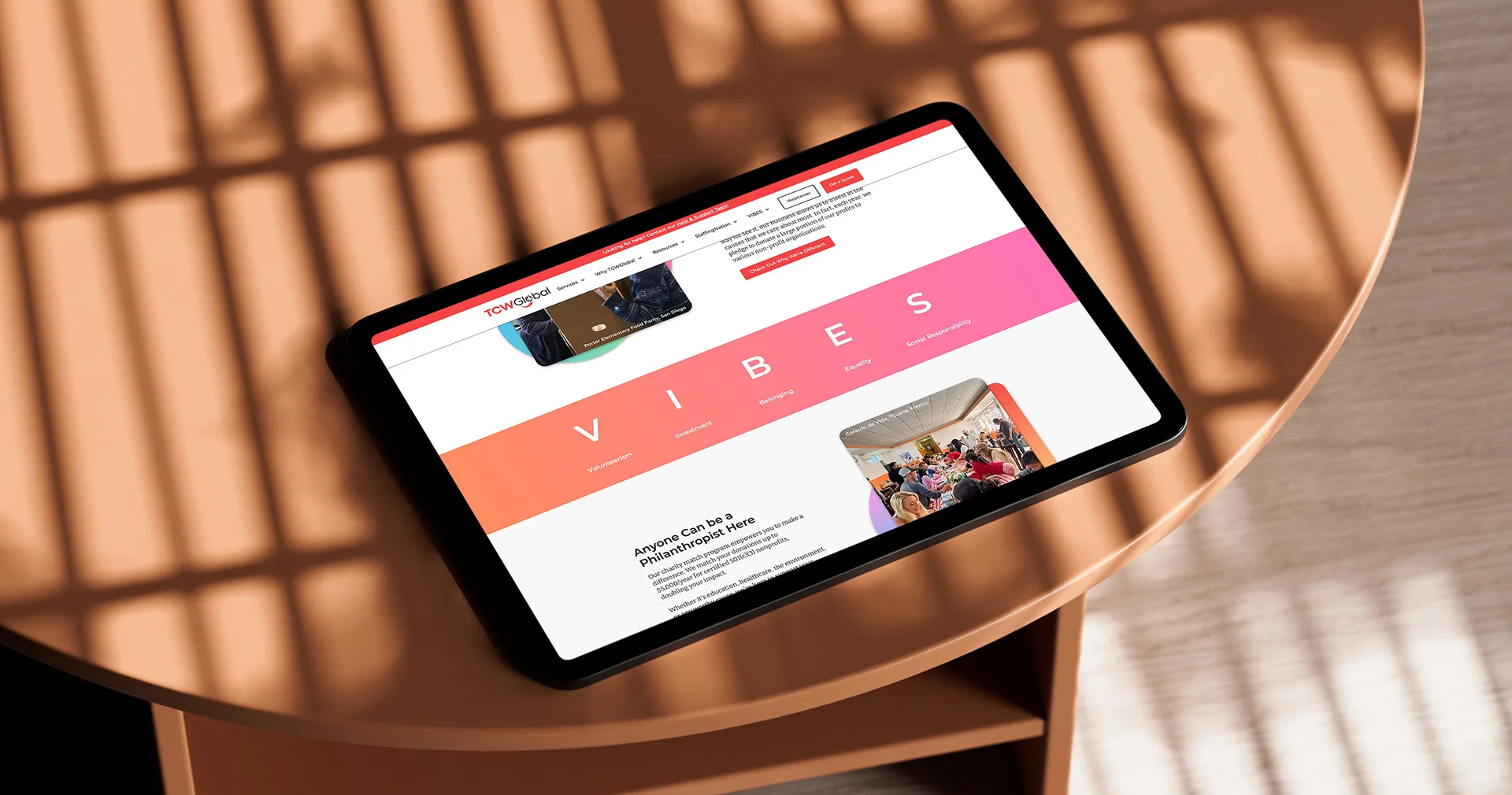 iPad mockup on a wood table displaying TCWGlobal's colorful VIBES volunteer and philanthropy landing page section