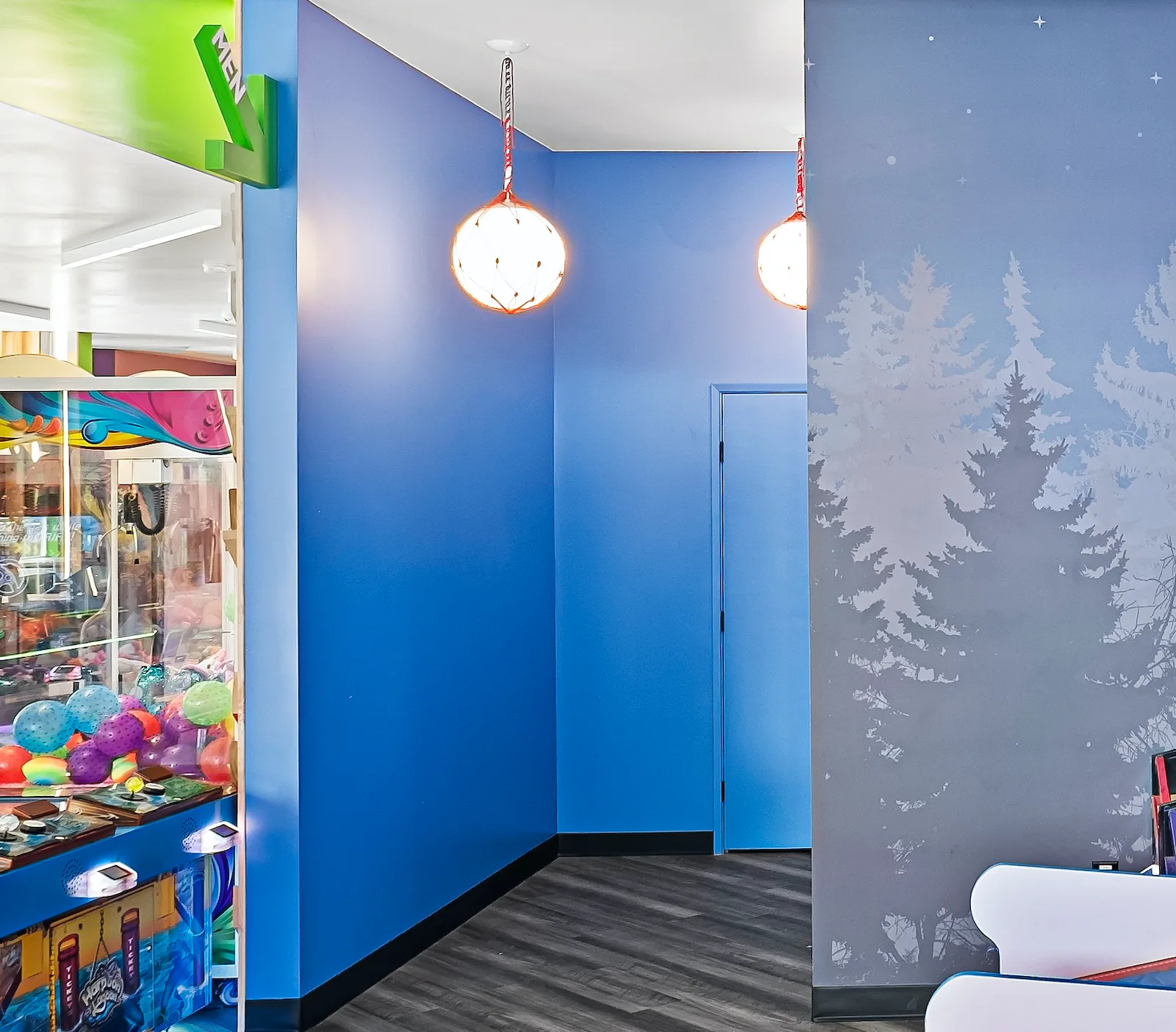 Arcade hallway with blue walls, illuminated pendant lights, and a moonlit forest mural leading to restrooms