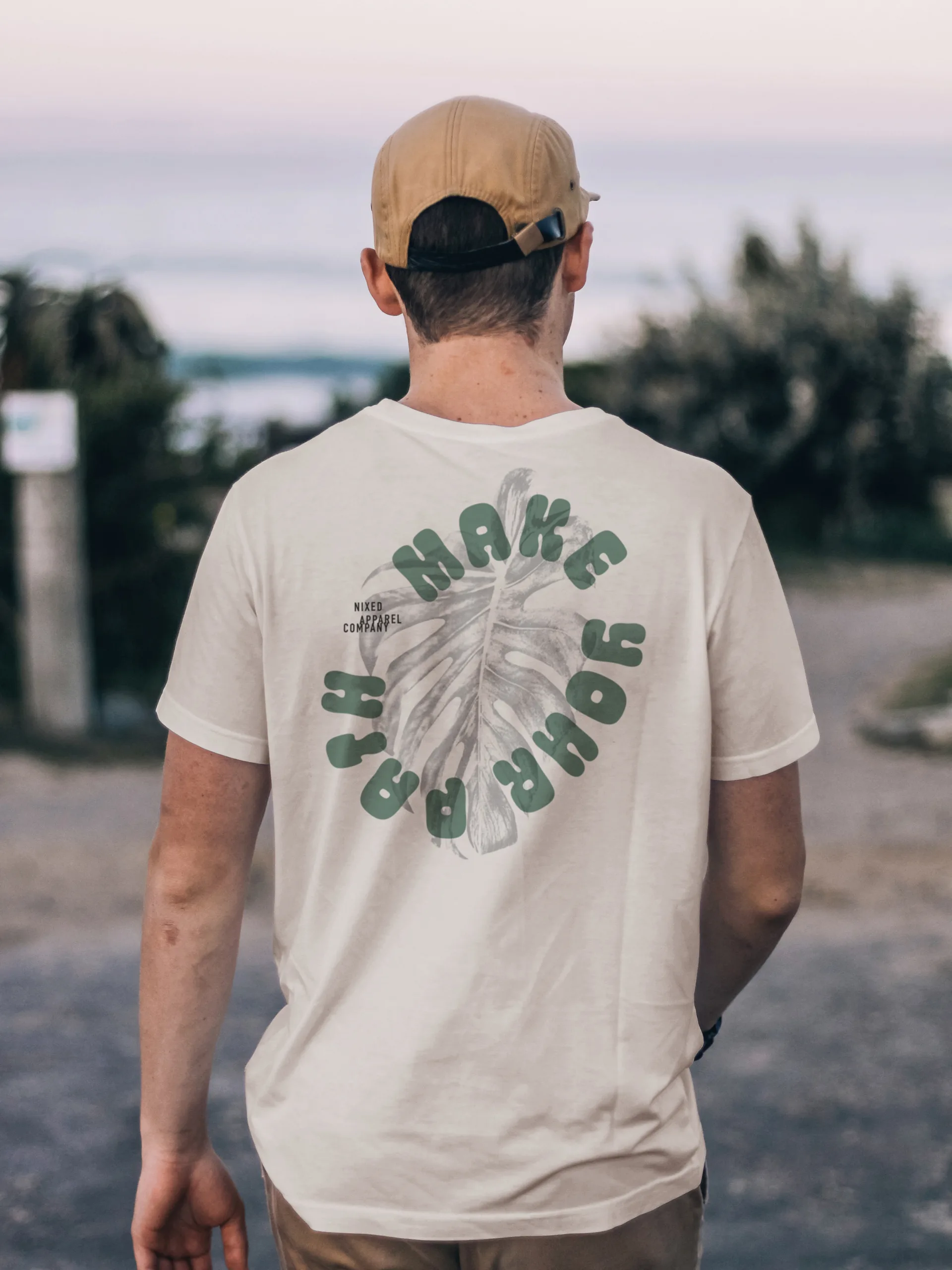 Man's back in a cream NIXED tee with Make Your Path text circling a monstera leaf print