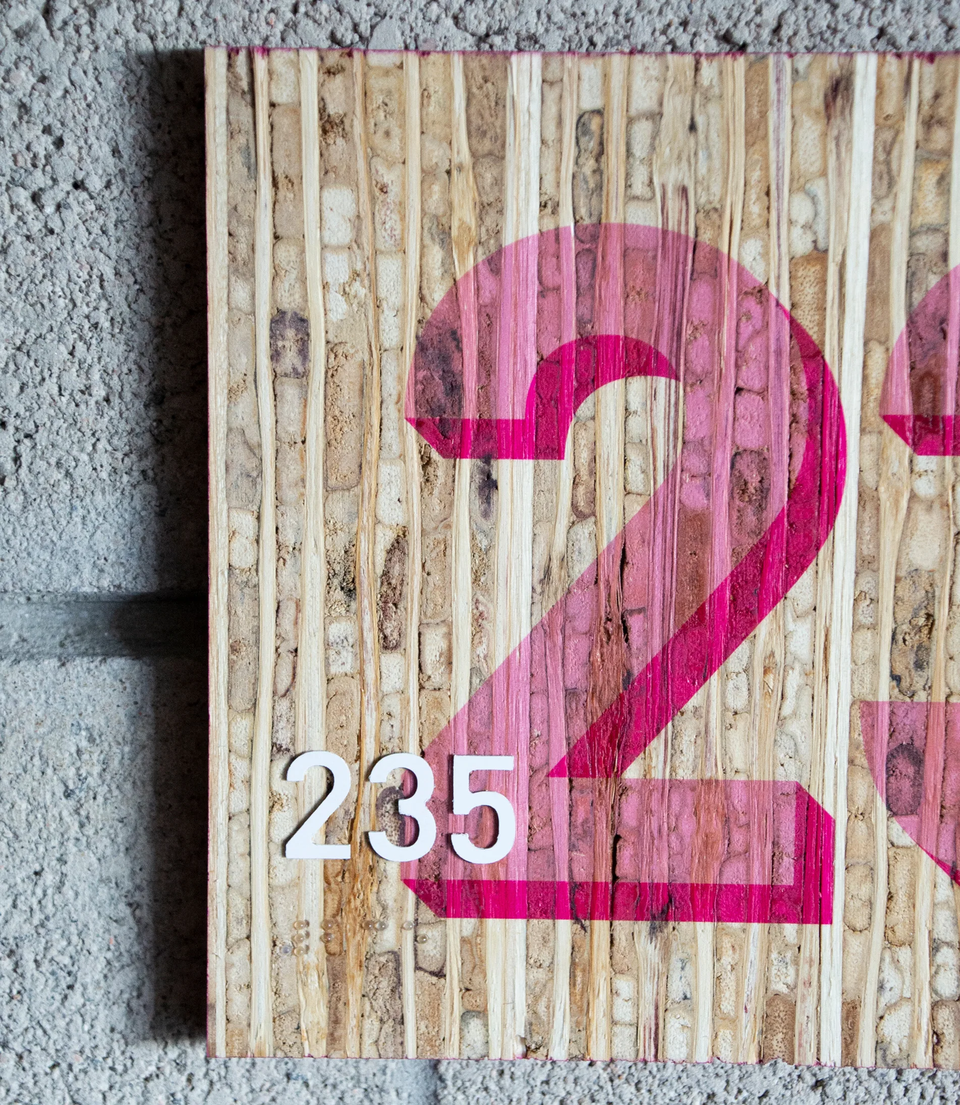 Close-up detail of the room 235 wood-grain sign showing the pink numeral overlap and small white number tag