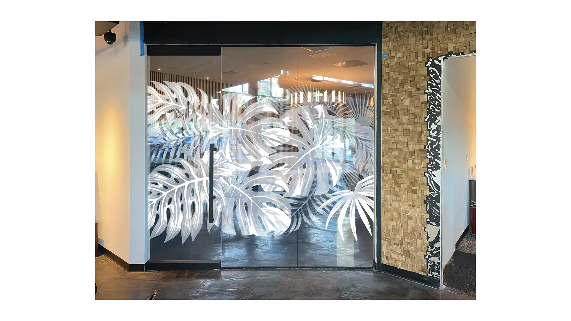 BoujieMana entrance with a frosted glass monstera-leaf treatment on the doors beside a textured accent wall