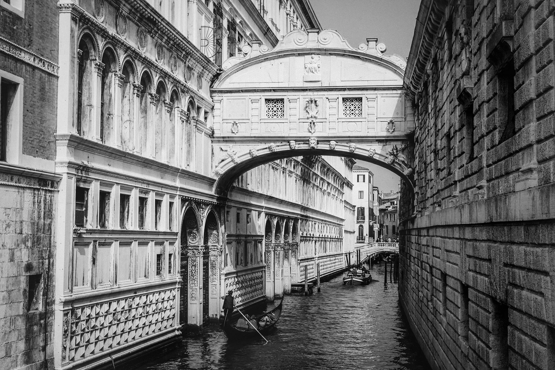 Black-and-white photo of Venice's Bridge of Sighs arching over a canal with a gondolier below