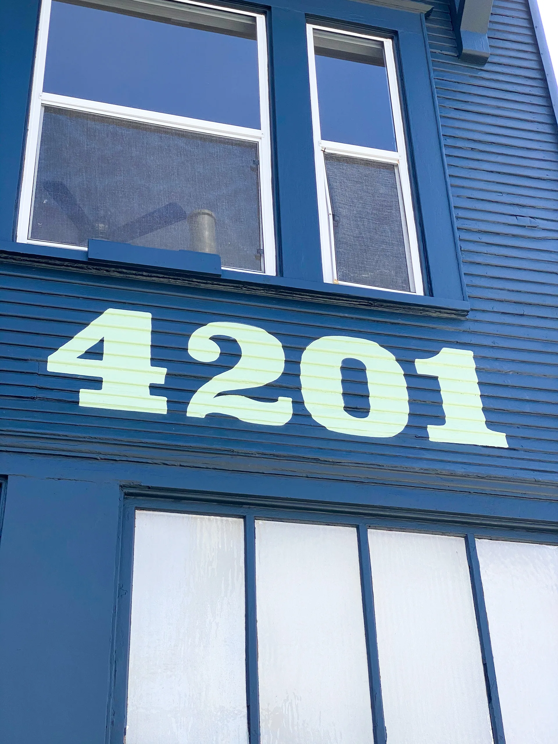 Mint green 4201 address numbers painted on navy blue upper-story siding above the storefront windows