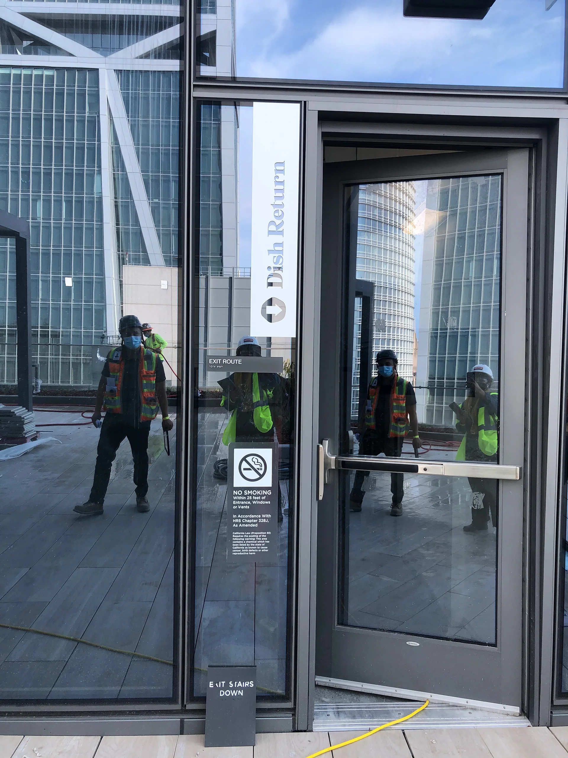 Dish Return blade sign on an exterior terrace door, with construction workers reflected in the glass