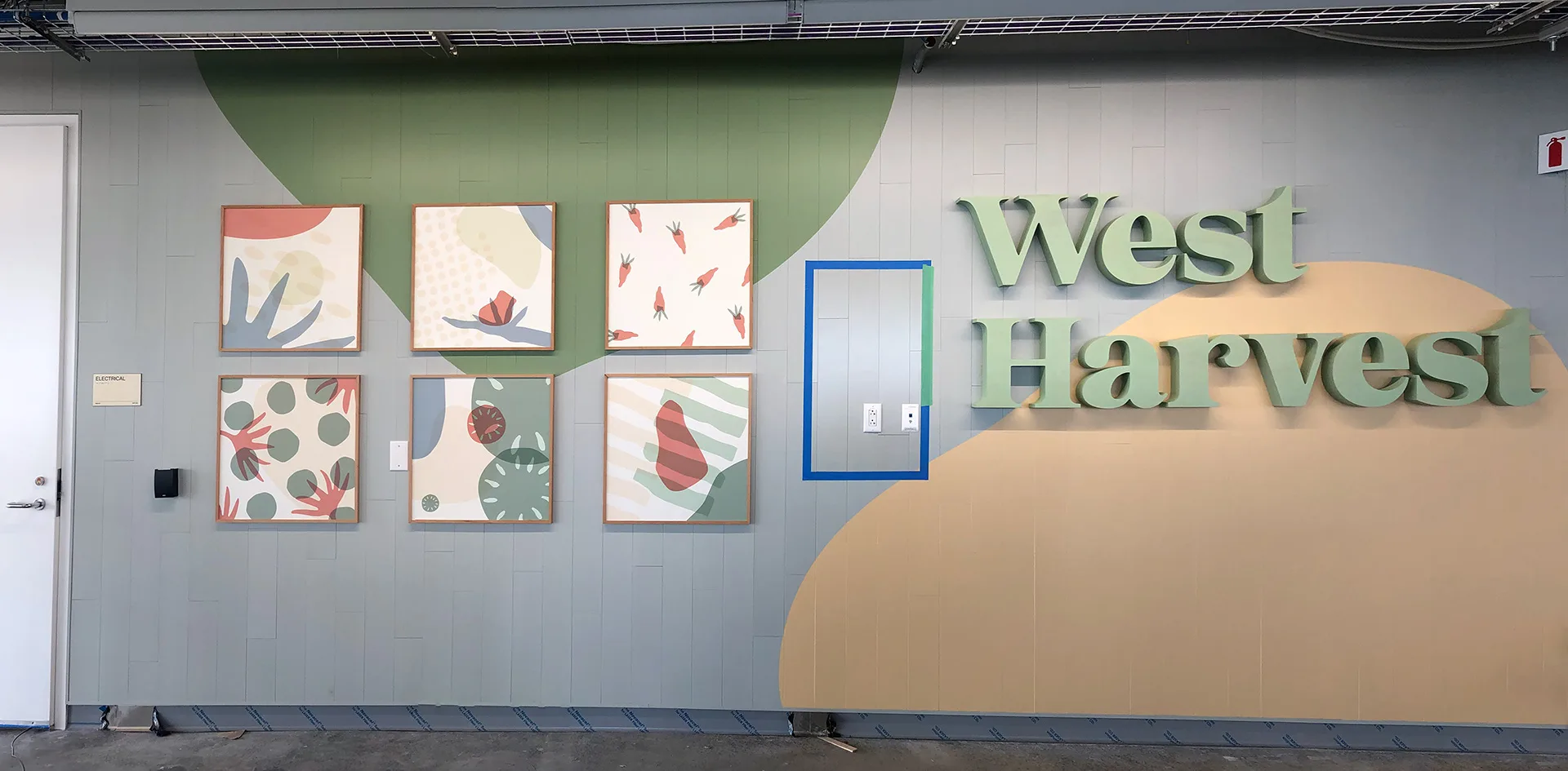West Harvest dimensional wall sign above six framed produce-pattern art prints on a painted mural wall