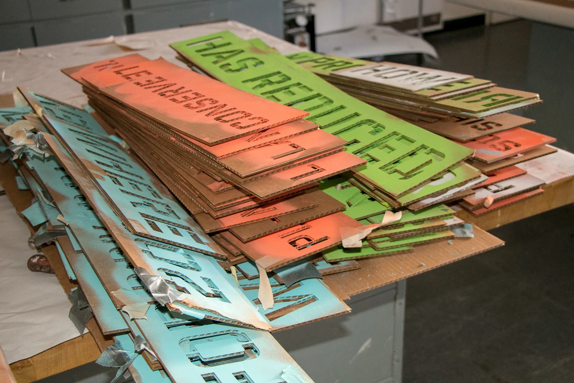 Pile of cut cardboard letter stencils in green, orange, and teal used to paint the staircase messages