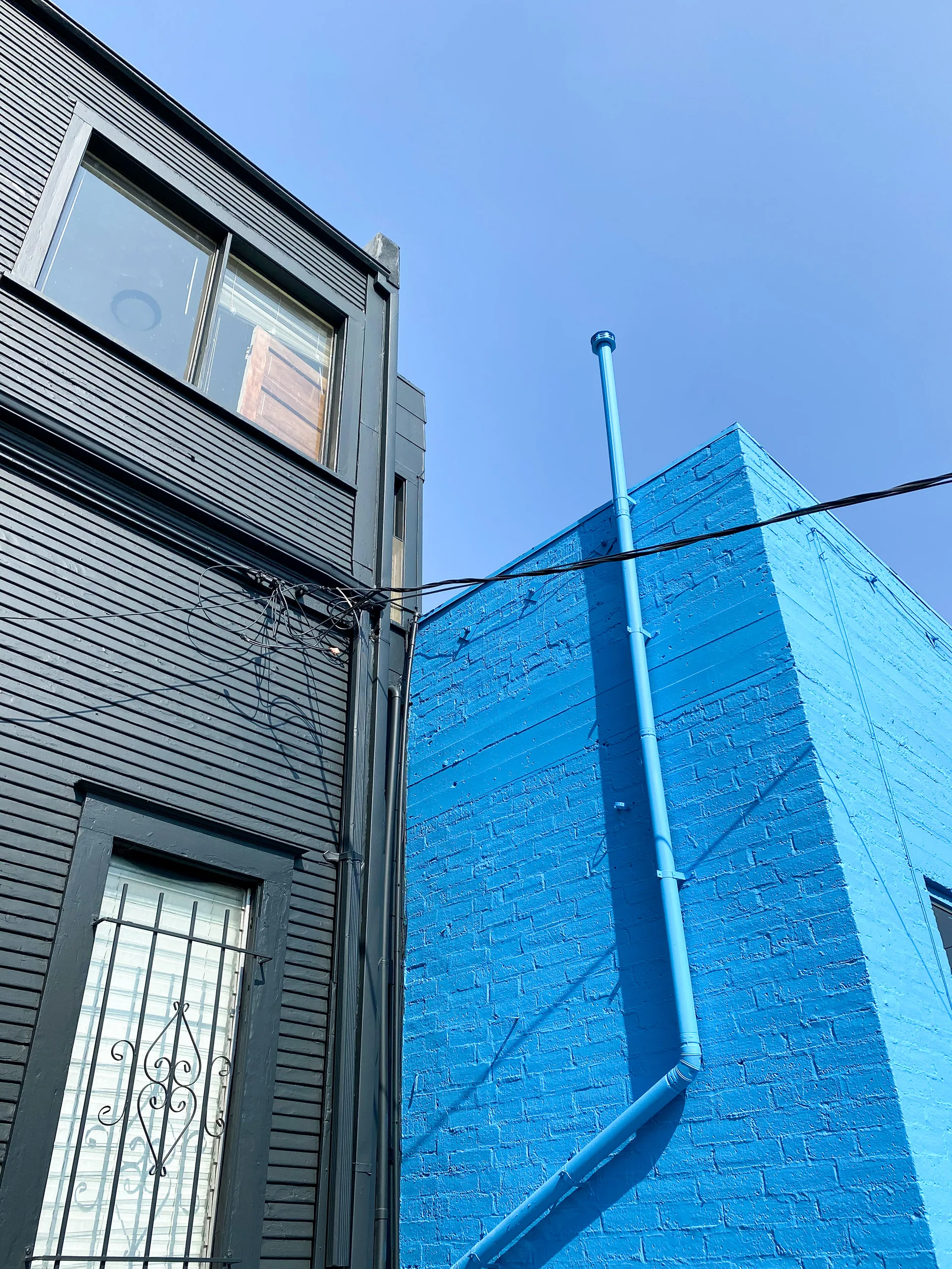 Dark charcoal building corner beside a bright blue painted brick wall with a matching blue conduit pipe