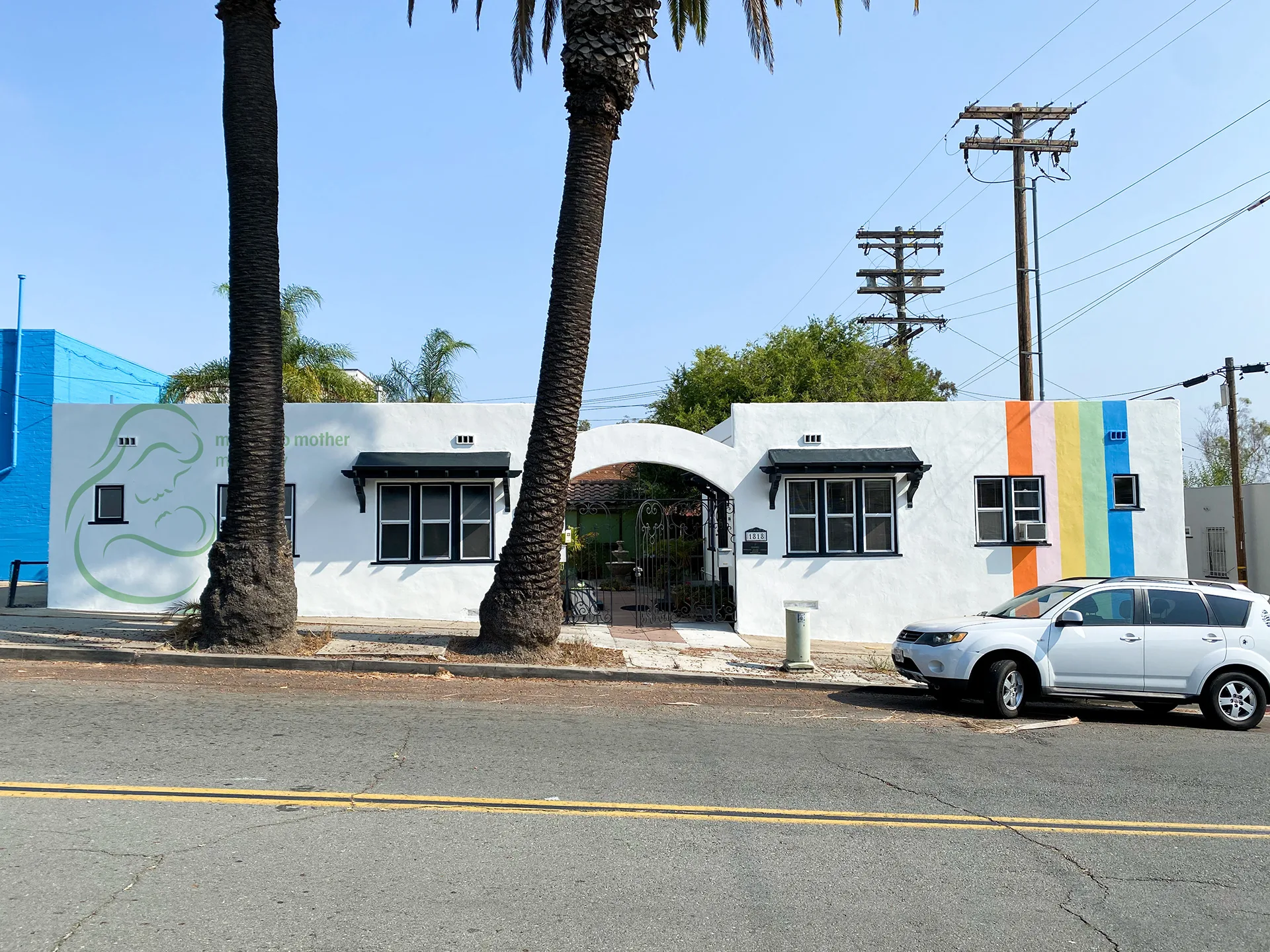 Mother to Mother Midwifery building with its logo mural, palm trees, and the rainbow-striped building corner beyond