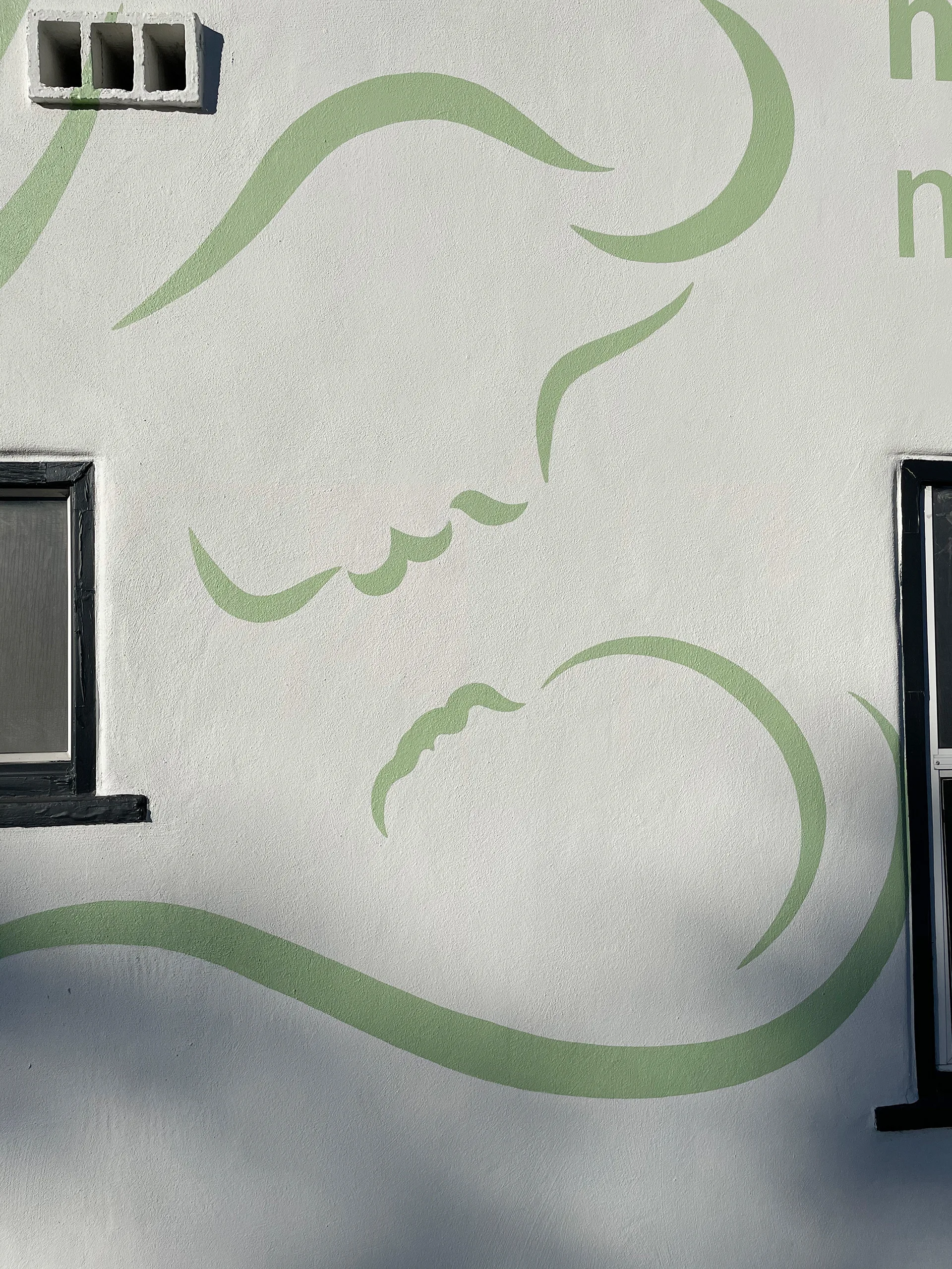 Close-up of the green line-art mother-and-child logo painted on the midwifery building's stucco wall