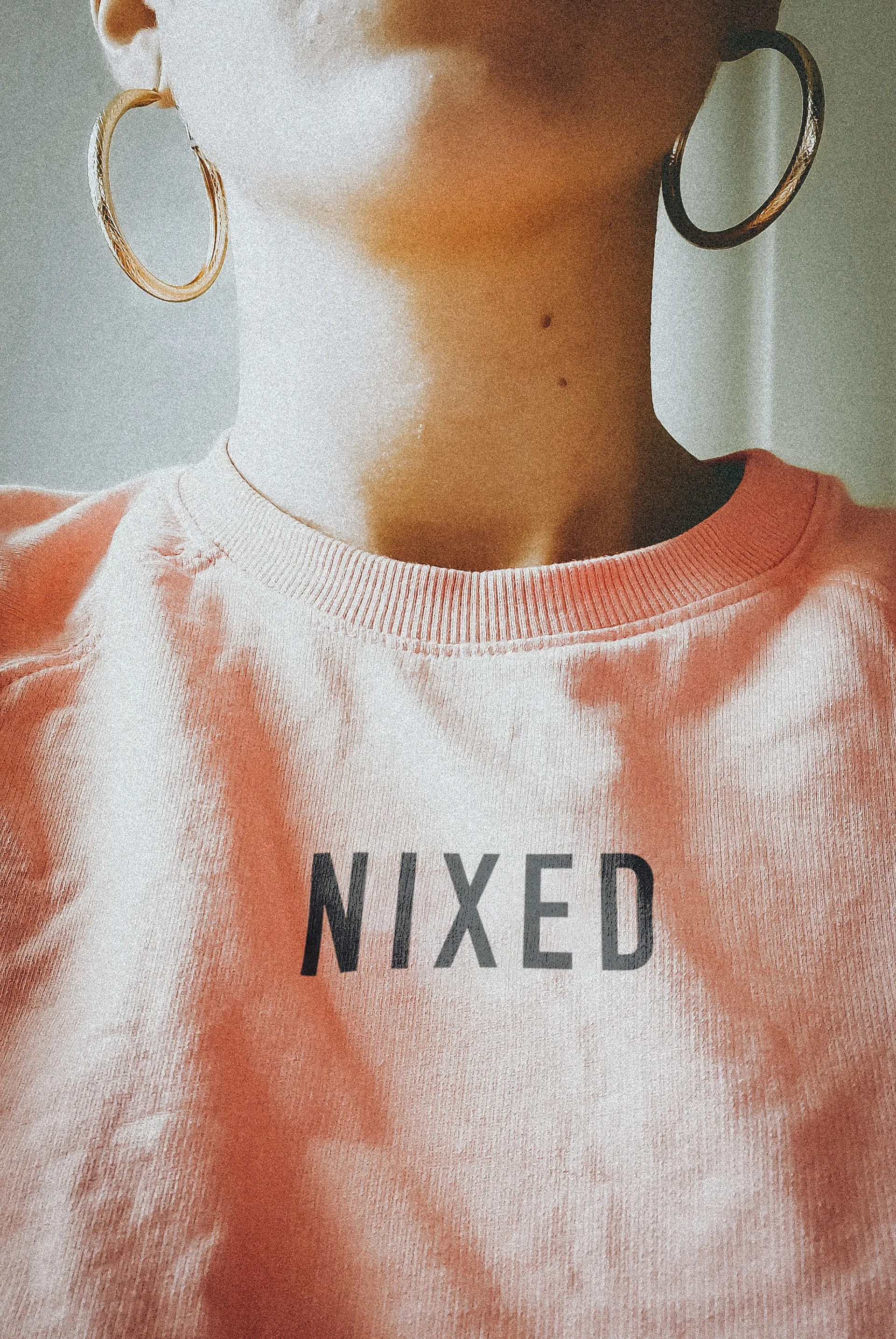 Close-up of a woman in a peach tie-dye NIXED sweatshirt with a bold wordmark across the chest