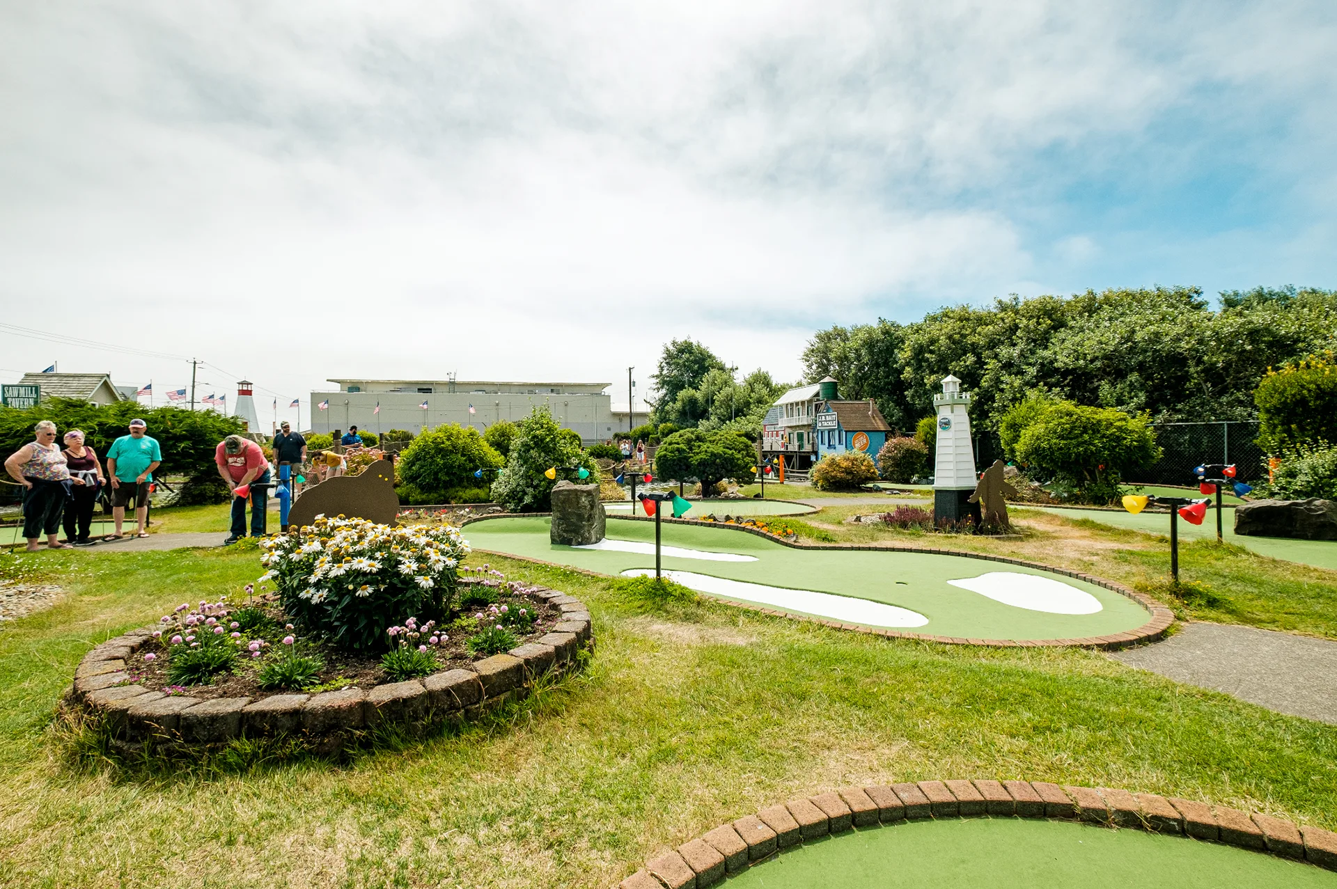 Mini golf course with families putting among landscaped flower beds and a stone marker in the distance