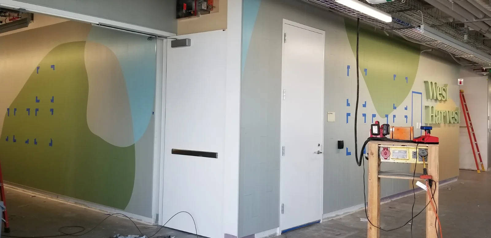 West Harvest wall mural and dimensional sign under construction, with painted color blocking on wall panels
