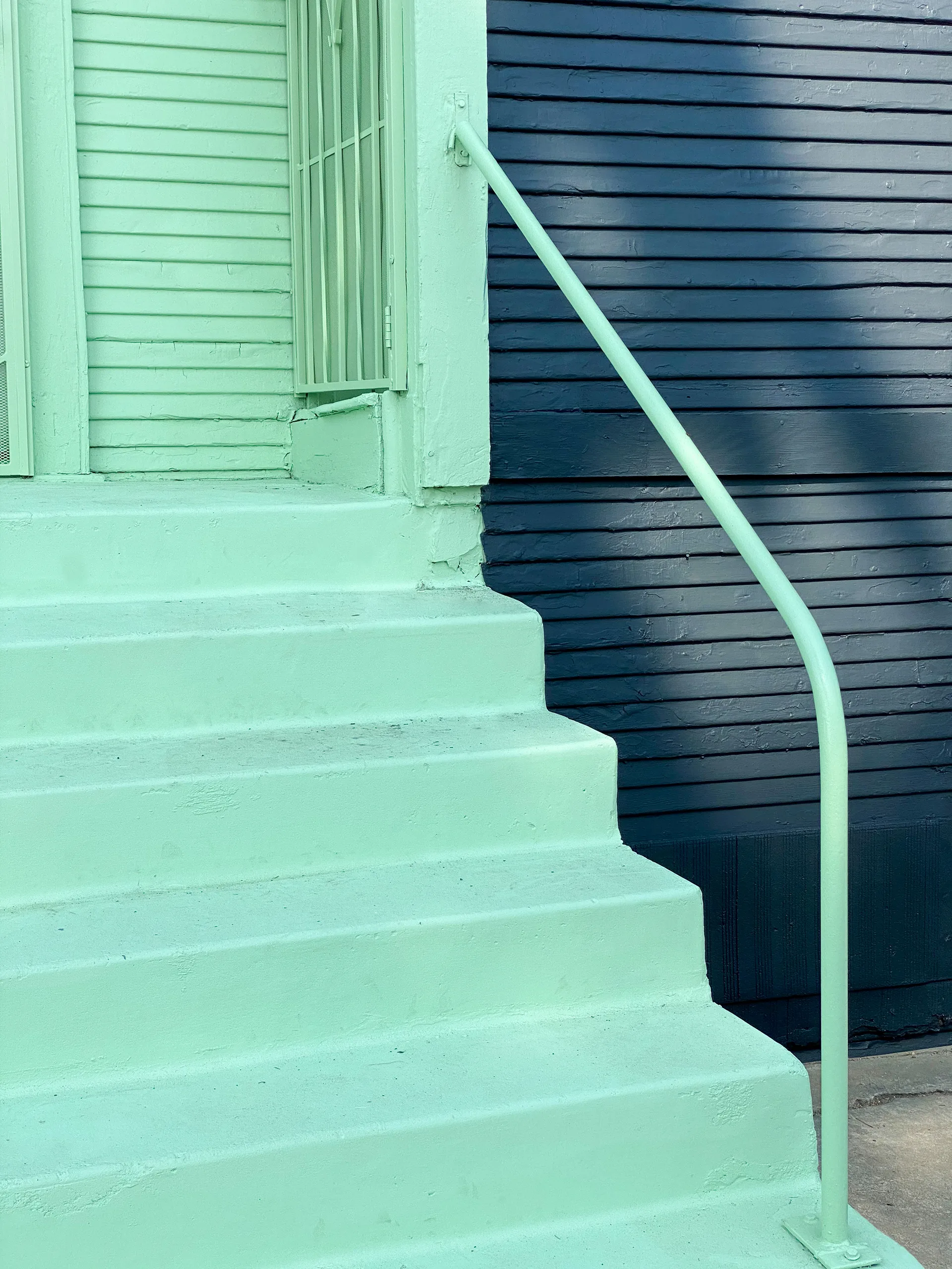 Mint green painted concrete stairs and handrail leading up to a matching green entry door