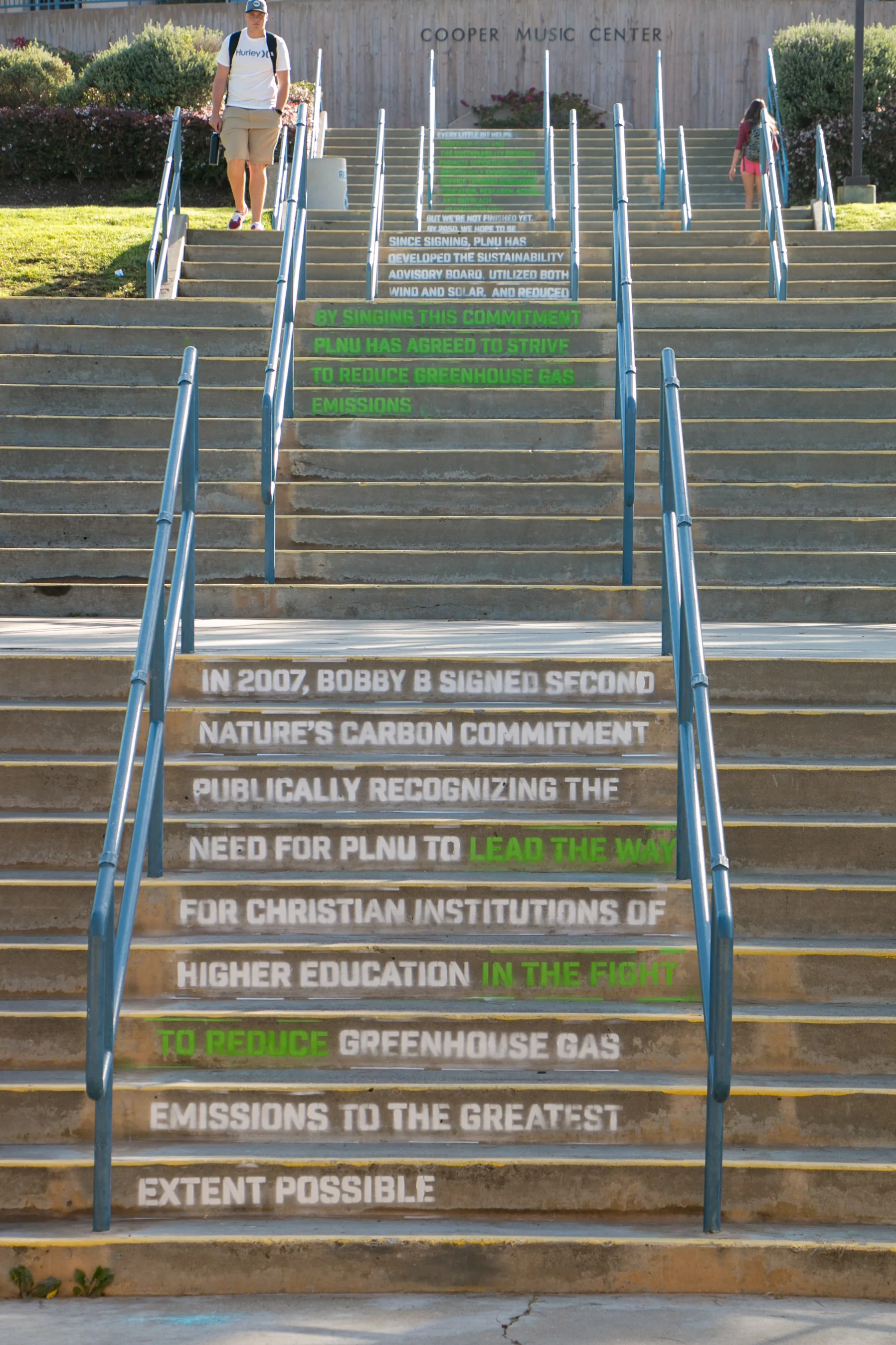 Wide staircase at Cooper Music Center stenciled with white and green text about PLNU's 2007 carbon commitment pledge
