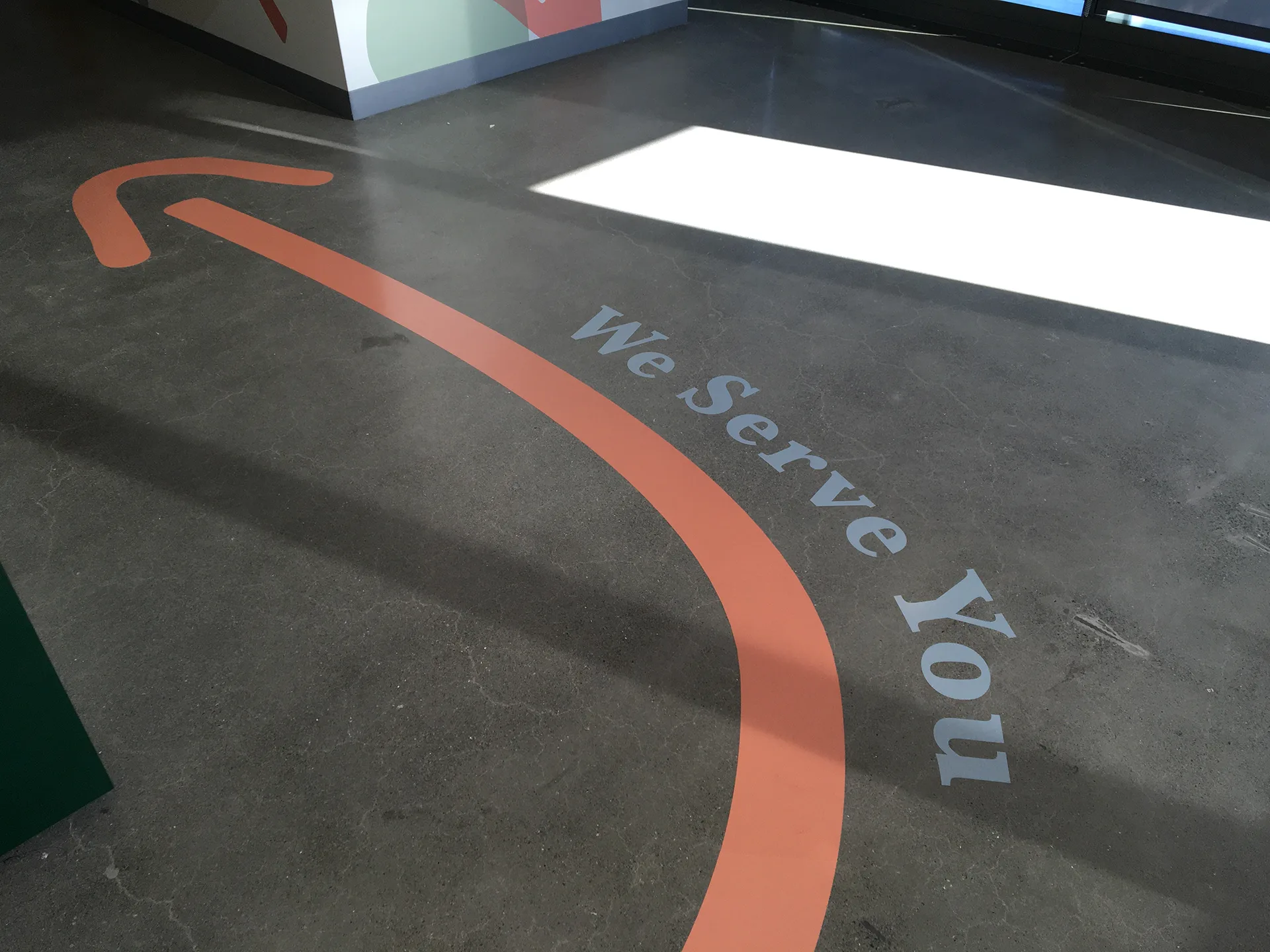 We Serve You wayfinding arrow on the cafe floor pointing toward the digital menu board