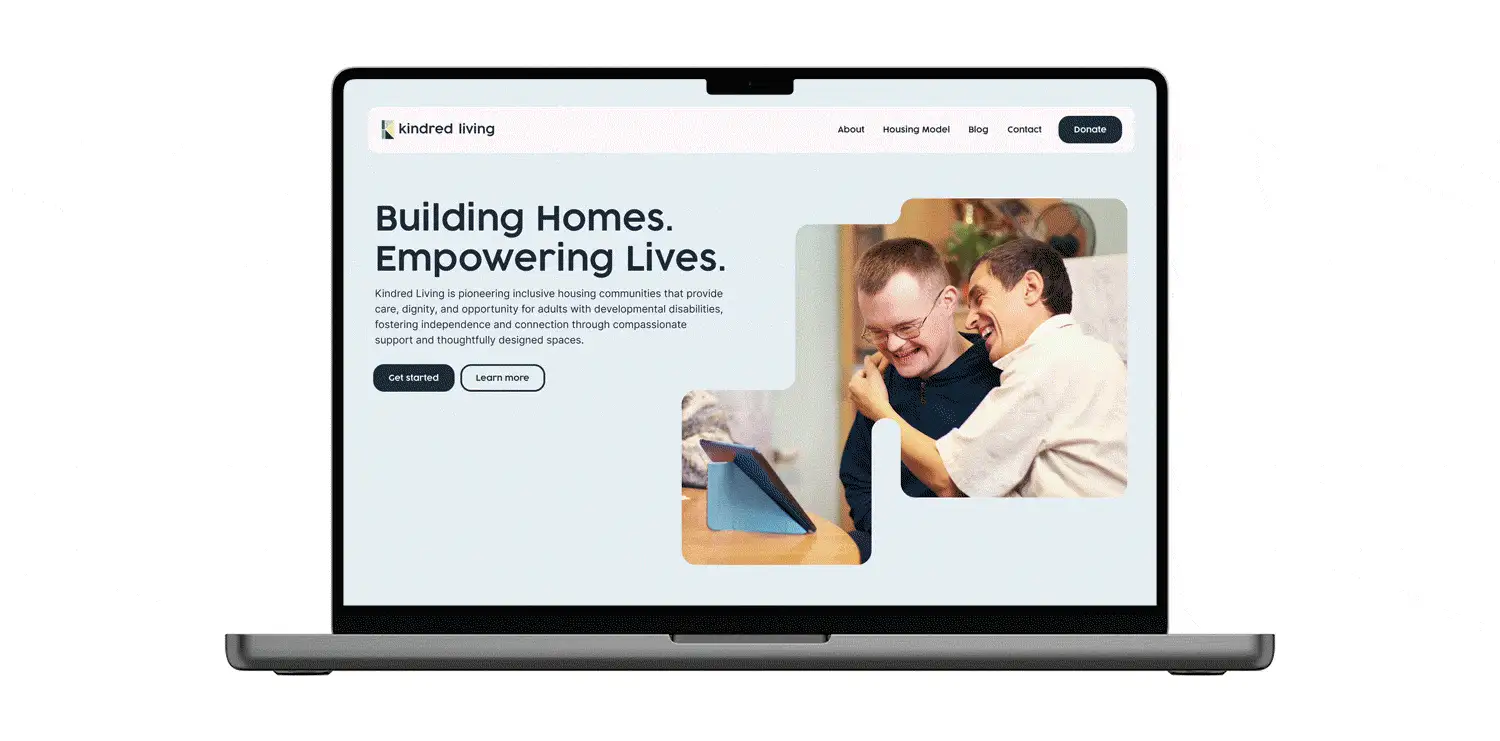 Laptop displaying the Kindred Living homepage hero reading Building Homes, Empowering Lives, with two men laughing together