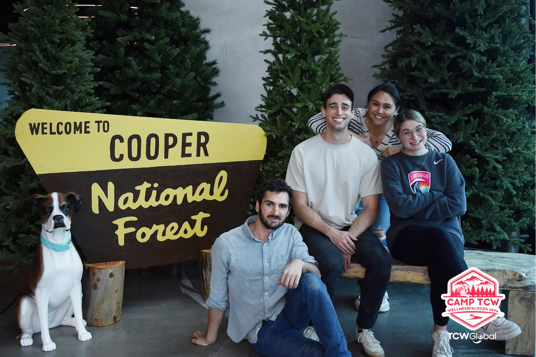 Four people and a dog posing beside a Welcome to Cooper National Forest sign at the Camp TCW WellnessPalooza event