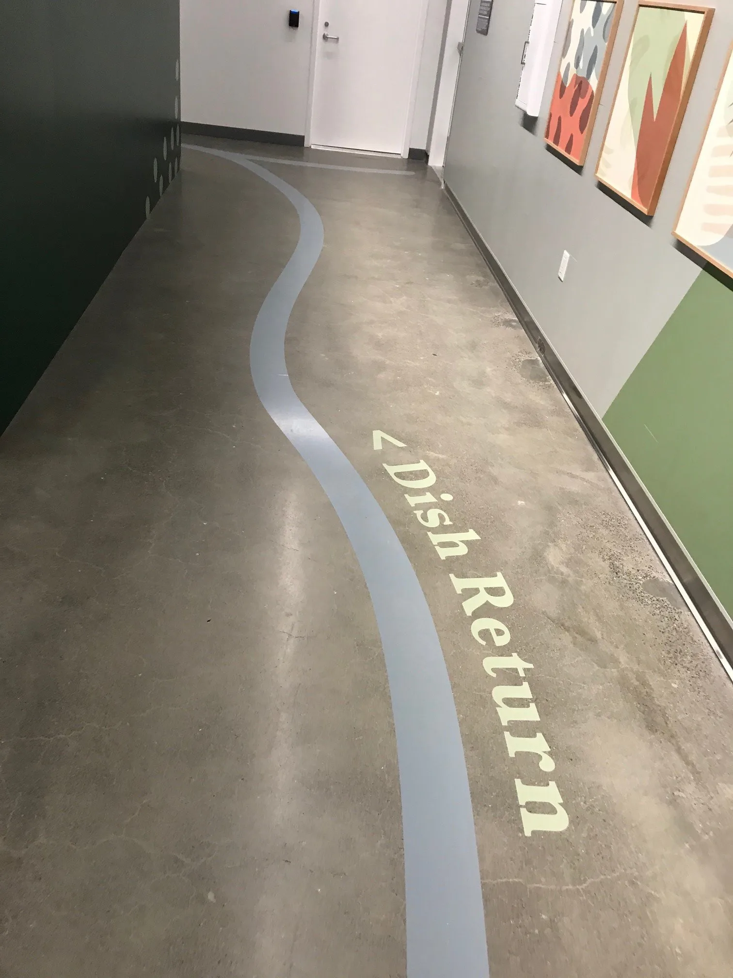 Dish Return floor graphic leading down a hallway past framed produce-pattern art at West Harvest