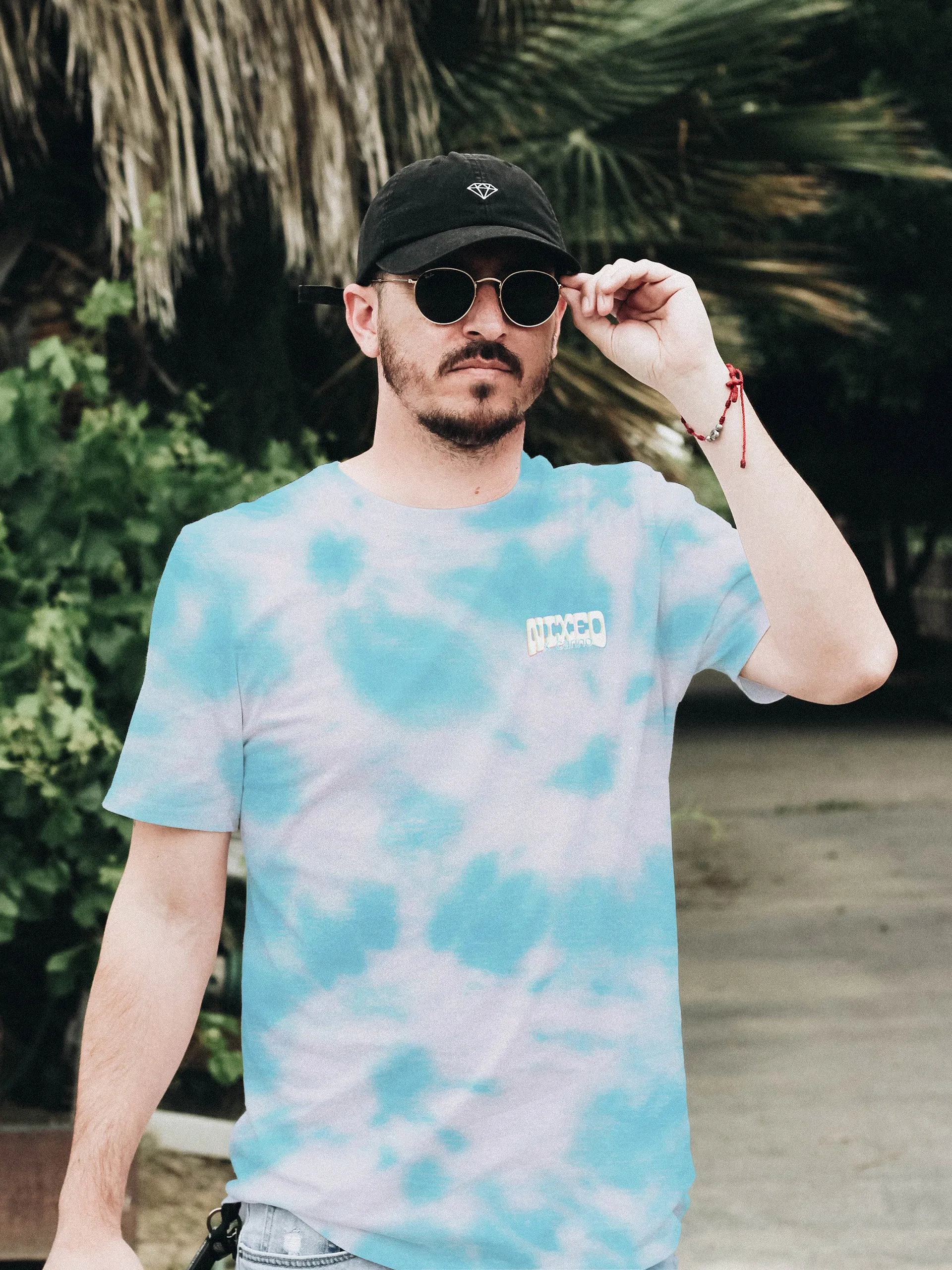 Man in sunglasses and a cap wearing a teal tie-dye NIXED tee with a small chest wordmark