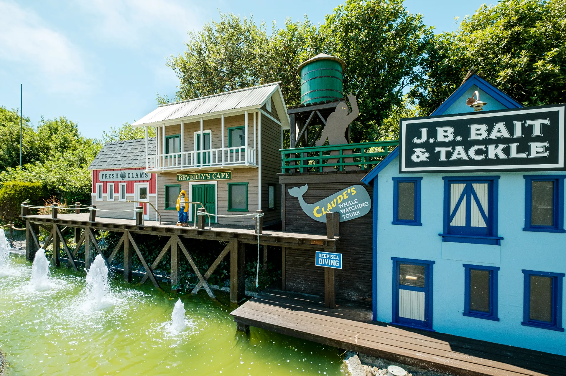 Mini golf village facades for Fresh Clams, Beverly's Cafe, and J.B. Bait & Tackle above a fountain-filled pond