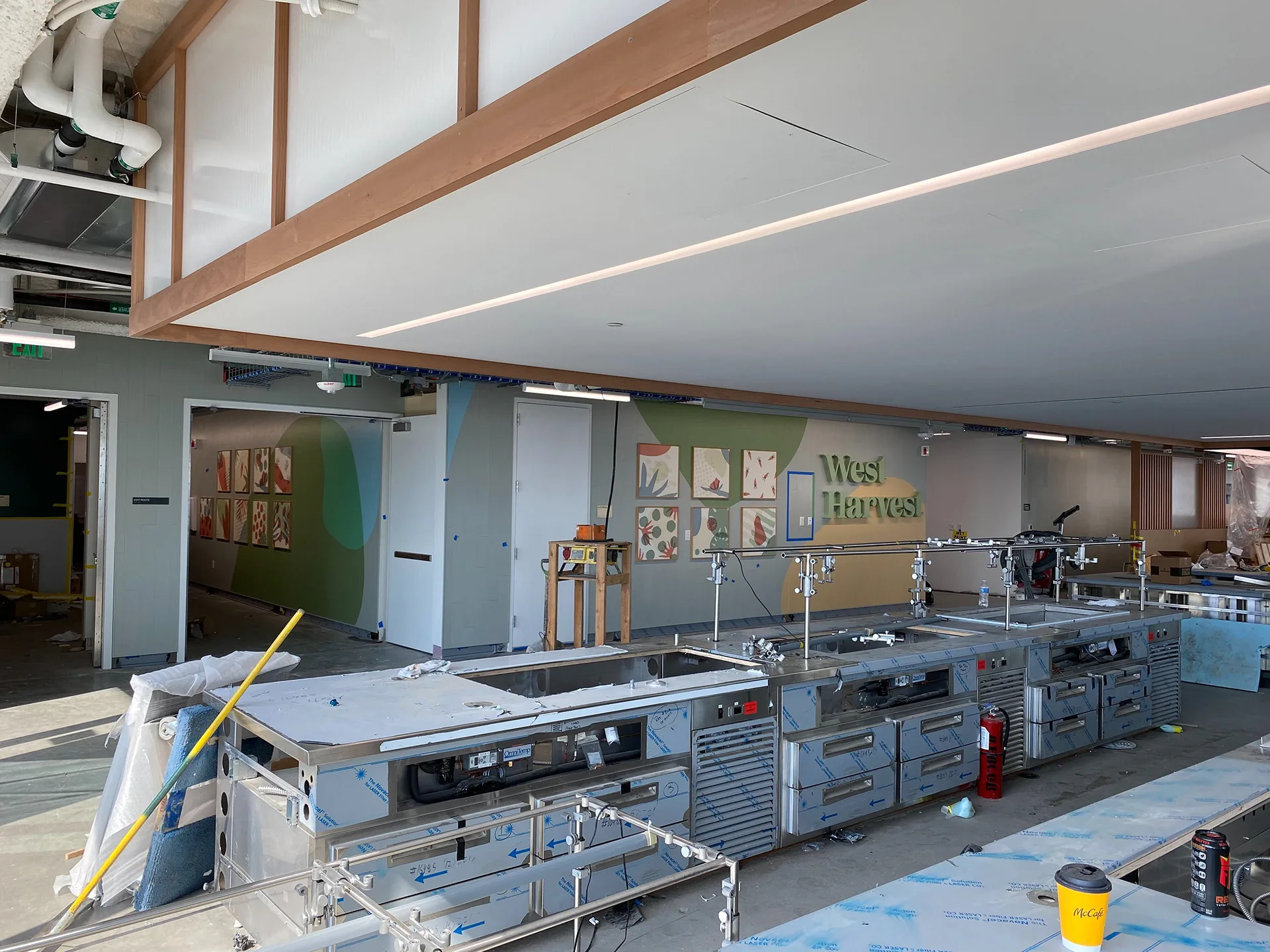 Stainless steel serving line under construction with the West Harvest sign wall visible in the background