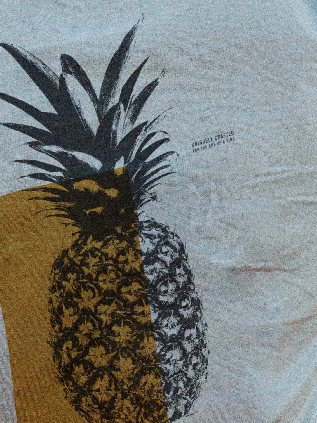 Close-up of a two-tone mustard and charcoal pineapple graphic on a light NIXED tee