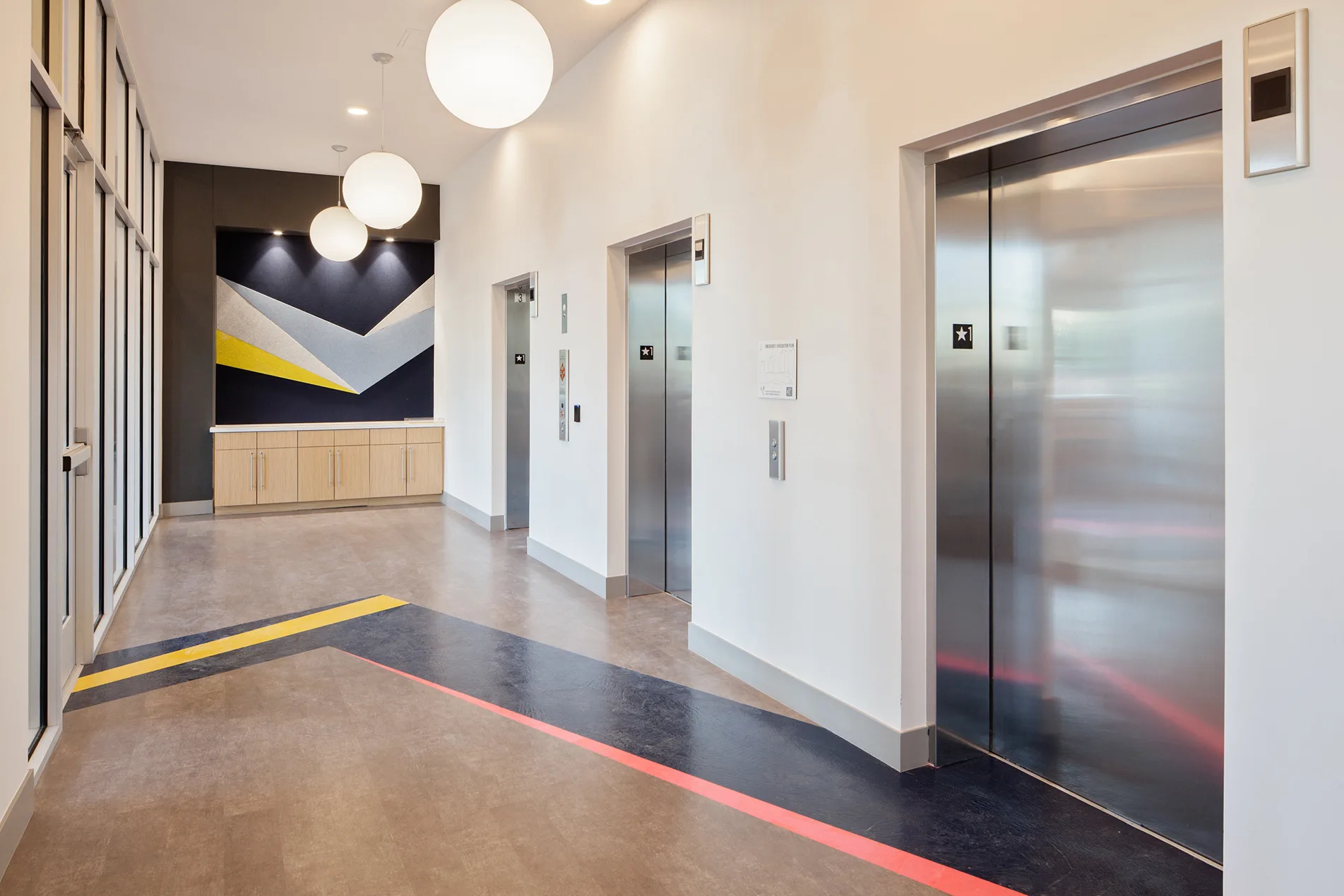 Student housing elevator lobby with globe pendant lights, a geometric navy and yellow mural, and colored floor stripes