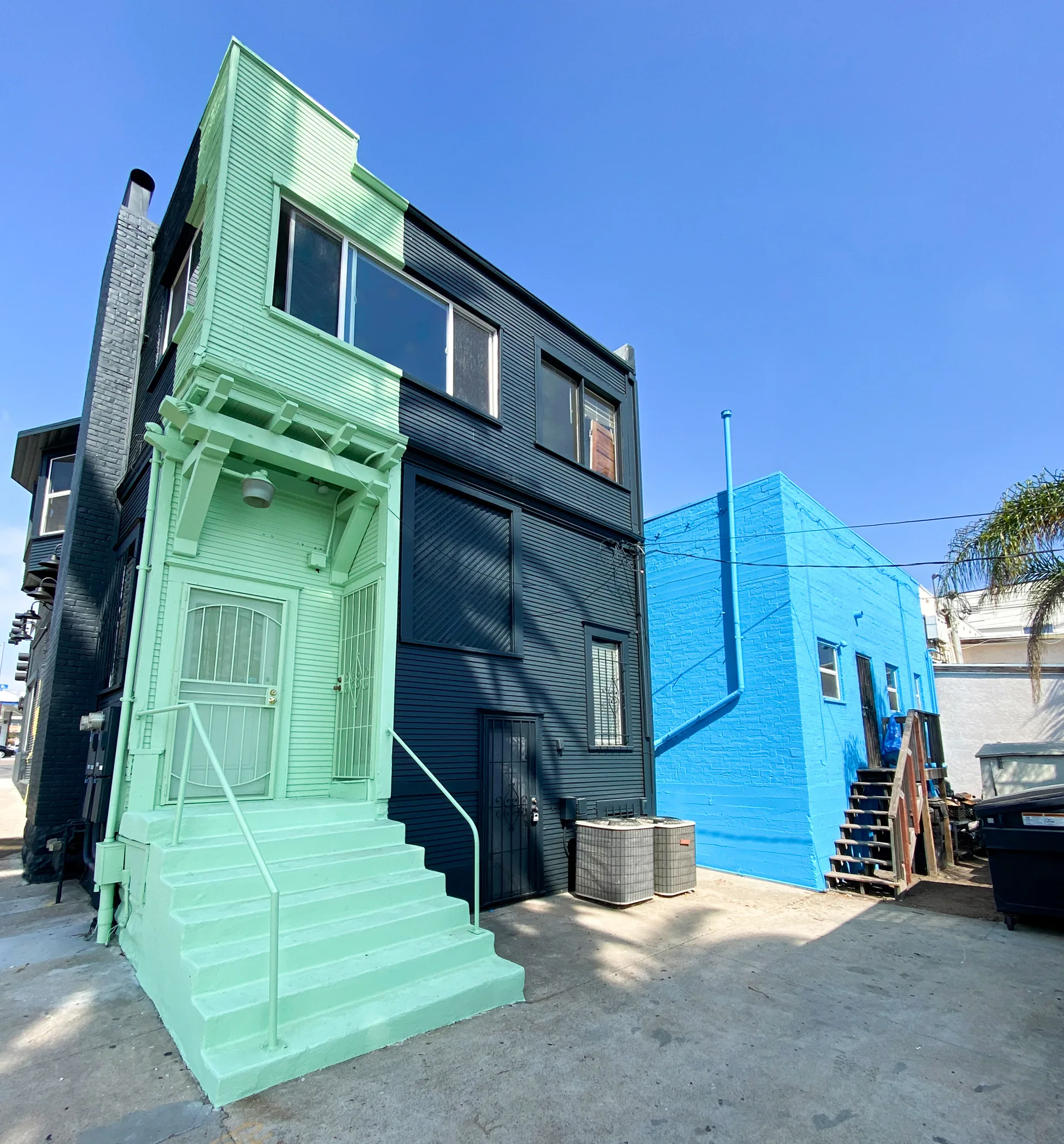 Row of mint green, navy, and bright blue painted building facades seen from the parking lot side
